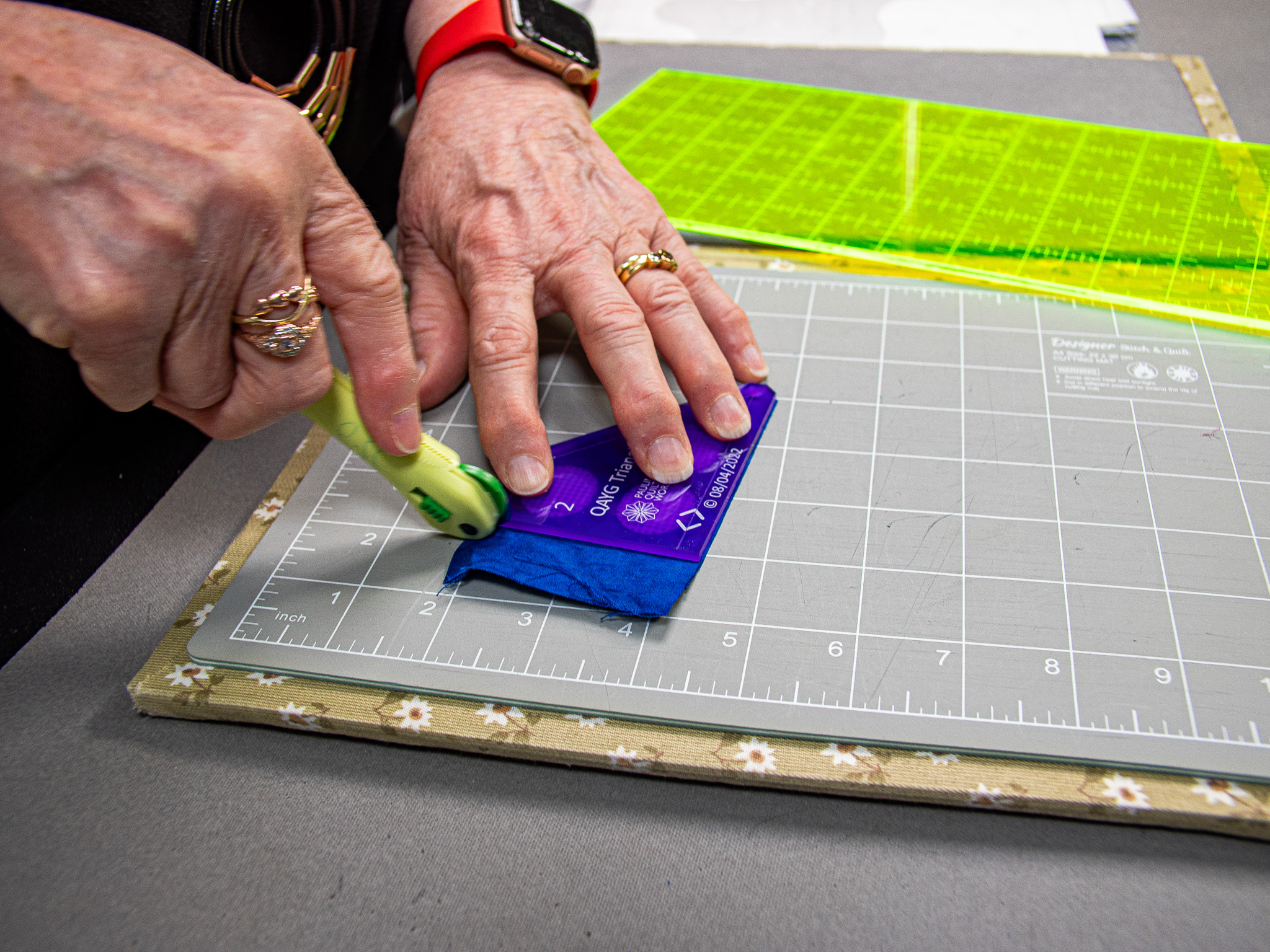 A person's hand applying firm, even pressure to a rotary cutter, moving it smoothly along a ruler.